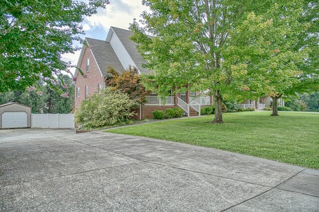 view of property hidden behind natural elements featuring brick siding, a detached garage, a porch, concrete driveway, and a front yard