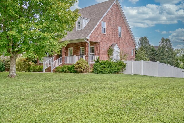 view of home's exterior with covered porch, brick siding, a lawn, and fence