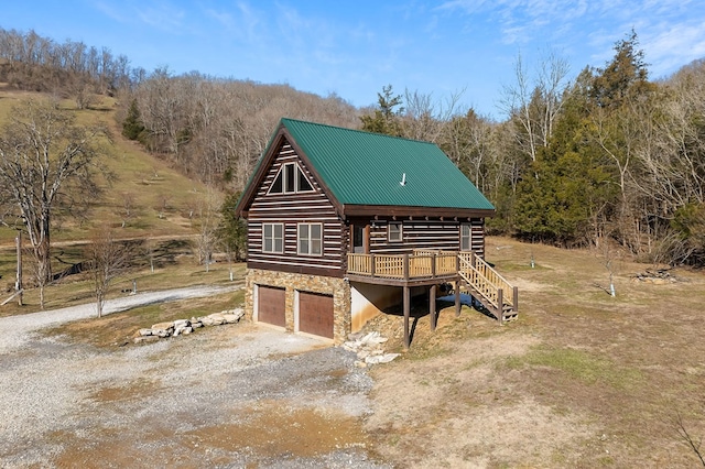 view of front of home featuring dirt driveway, an attached garage, metal roof, log exterior, and stone siding