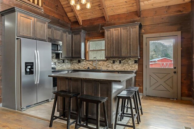 kitchen featuring vaulted ceiling with beams, stainless steel appliances, a sink, wood ceiling, and a center island