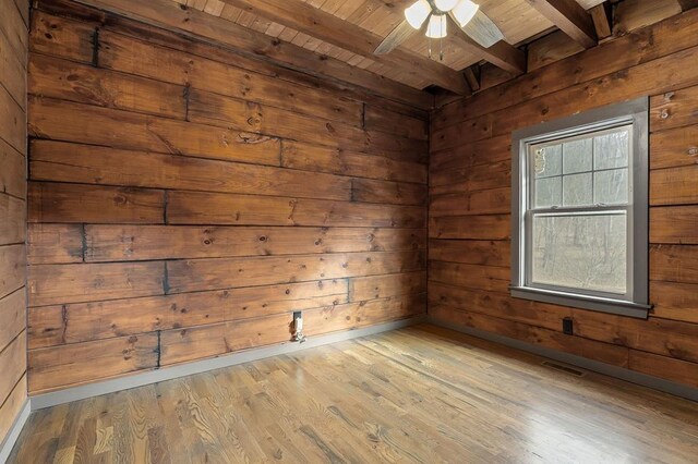 unfurnished room with wood walls, beamed ceiling, and light wood-style floors