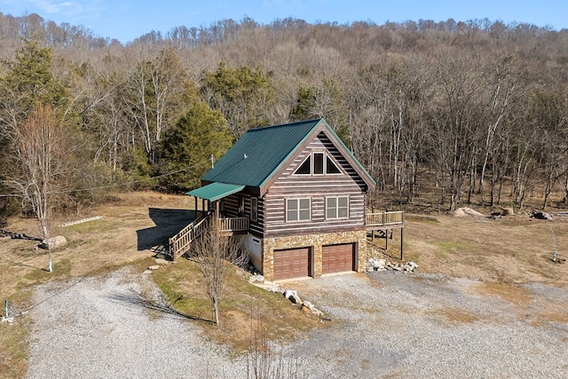 view of front of home featuring stone siding, driveway, a forest view, and an attached garage