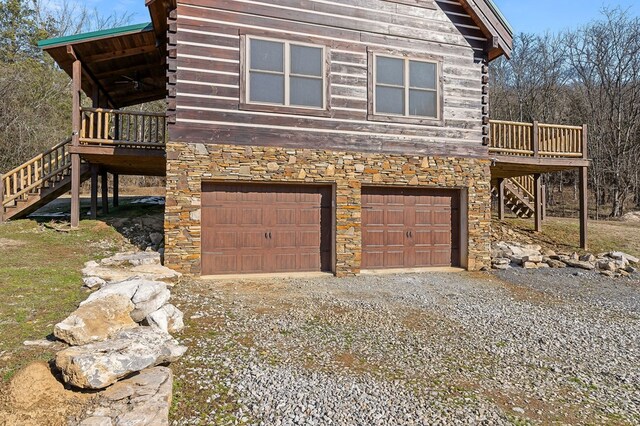 view of side of property featuring driveway, stone siding, log siding, an attached garage, and stairs