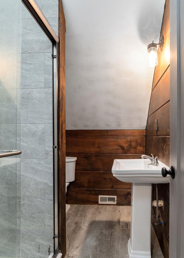 bathroom featuring wood finished floors, wood walls, a shower stall, and visible vents