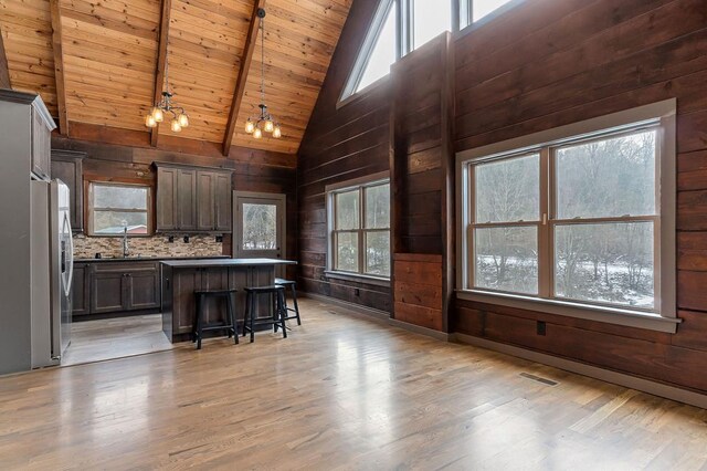 kitchen featuring wood walls, a sink, a kitchen breakfast bar, a center island, and pendant lighting