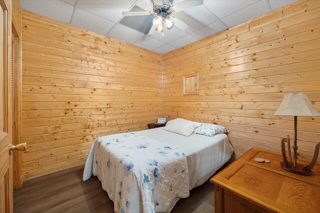 bedroom with ceiling fan, dark wood-type flooring, a paneled ceiling, and wooden walls