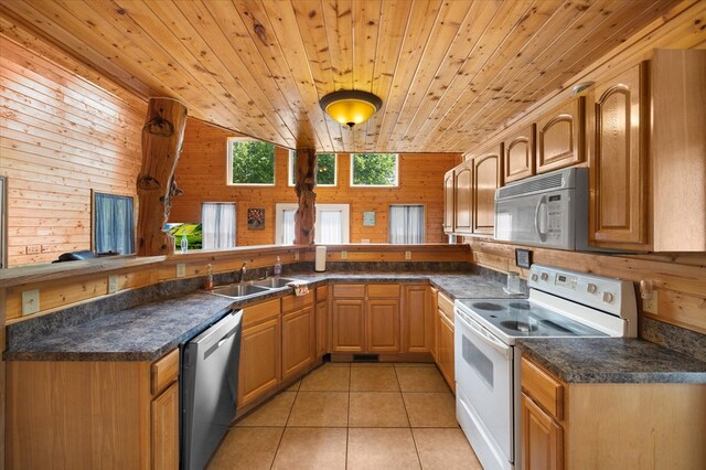 kitchen featuring light tile patterned flooring, wood walls, a sink, white appliances, and a peninsula