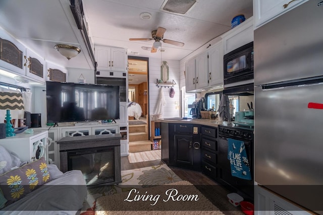 kitchen with light countertops, white cabinets, ceiling fan, black microwave, and stainless steel refrigerator