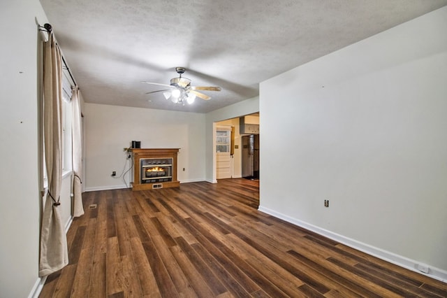 unfurnished living room featuring a textured ceiling, ceiling fan, dark wood-type flooring, baseboards, and a lit fireplace