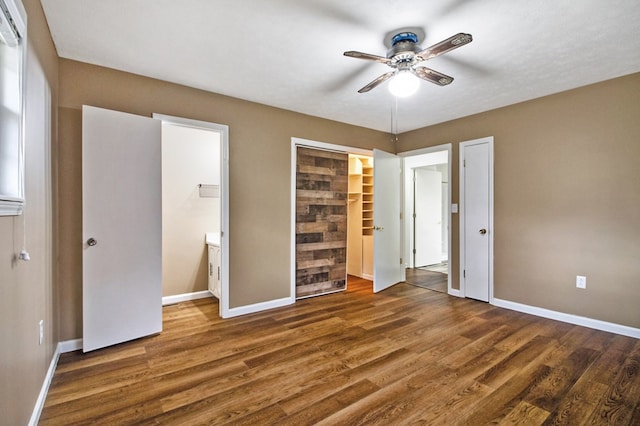 unfurnished bedroom featuring ensuite bathroom, ceiling fan, dark wood-style flooring, and baseboards