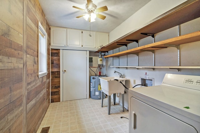 washroom featuring ceiling fan, electric water heater, wooden walls, visible vents, and cabinet space