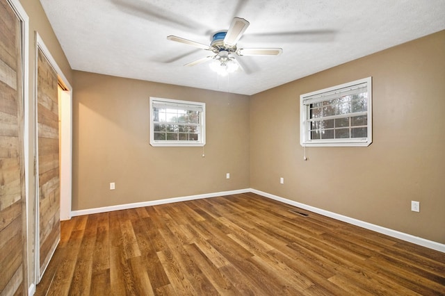 unfurnished bedroom featuring a textured ceiling, visible vents, a ceiling fan, baseboards, and dark wood-style floors