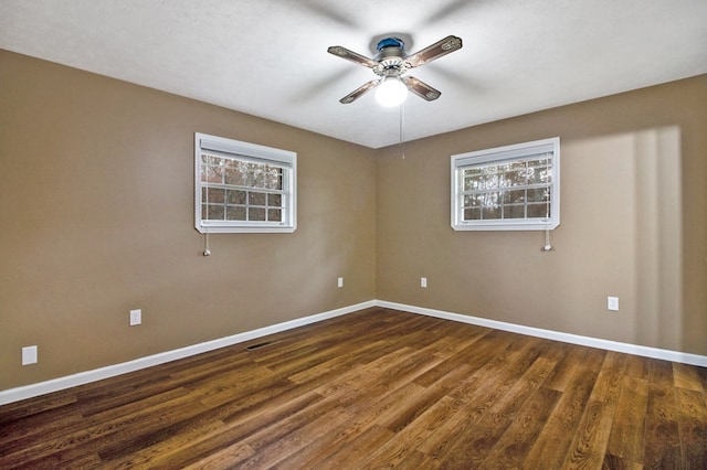 unfurnished room with dark wood-style floors, a ceiling fan, baseboards, and a wealth of natural light