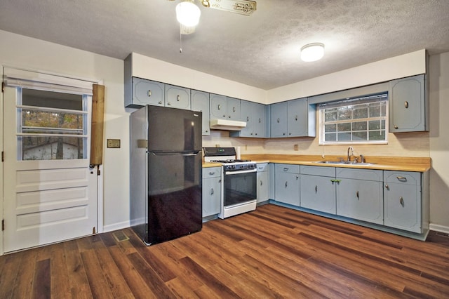 kitchen with under cabinet range hood, dark wood-style flooring, a sink, white range with gas cooktop, and freestanding refrigerator