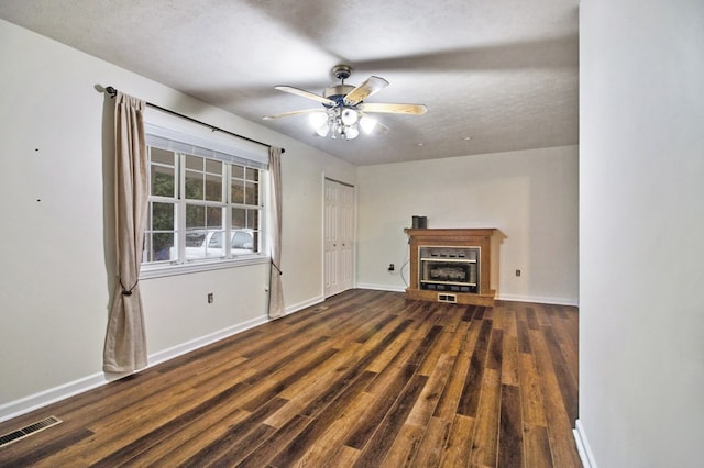 unfurnished living room with ceiling fan, dark wood-type flooring, a glass covered fireplace, and baseboards