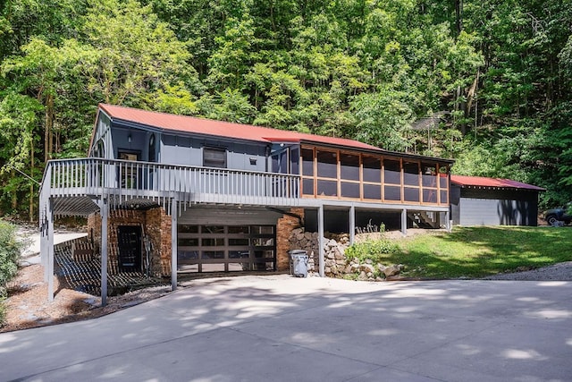 view of front of property with driveway, a garage, a view of trees, a sunroom, and metal roof