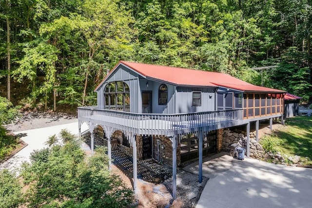 view of front of property with driveway, a garage, a sunroom, metal roof, and board and batten siding