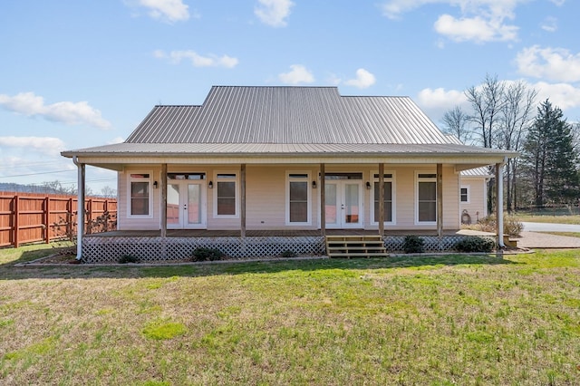 farmhouse with a front yard, fence, a porch, french doors, and metal roof