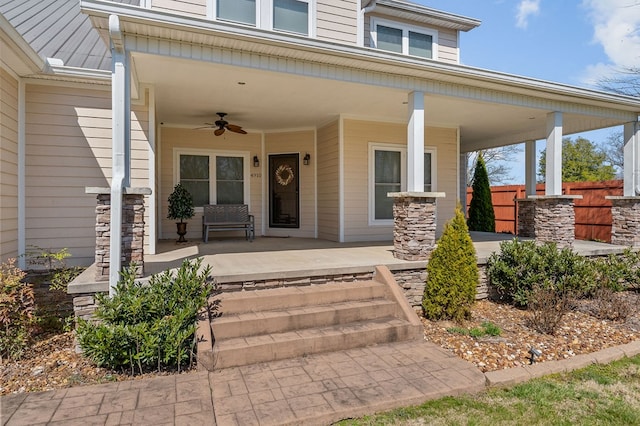 doorway to property with a porch, fence, stone siding, and ceiling fan