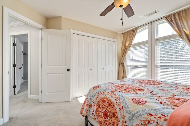 bedroom featuring visible vents, a closet, baseboards, light colored carpet, and ceiling fan