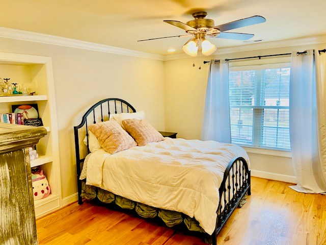 bedroom with light wood-type flooring, crown molding, and baseboards