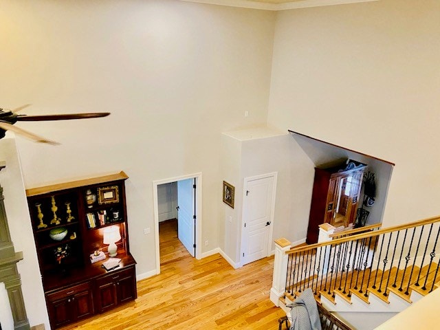 interior space with stairway, a towering ceiling, light wood-style floors, ceiling fan, and baseboards