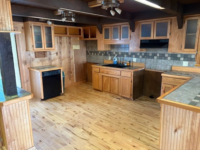 kitchen featuring under cabinet range hood, light wood-style floors, black dishwasher, tile counters, and glass insert cabinets