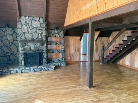 below grade area with a stone fireplace, wooden ceiling, wooden walls, wood finished floors, and stairs