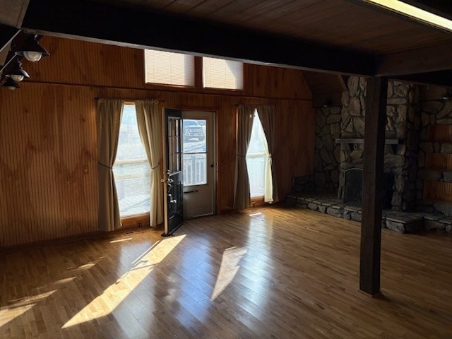 entrance foyer featuring a stone fireplace, wooden walls, wood finished floors, wood ceiling, and beam ceiling