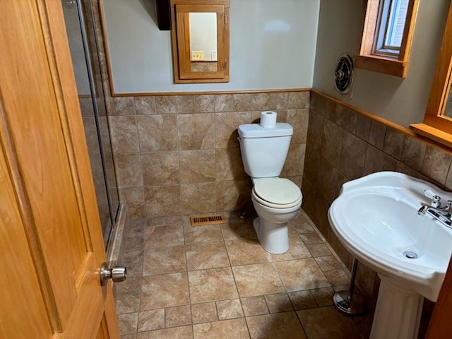 full bathroom featuring tile walls, wainscoting, toilet, an enclosed shower, and a sink