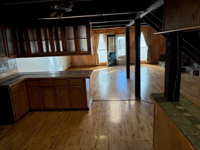 kitchen with glass insert cabinets, light wood-style floors, tile counters, and brown cabinets