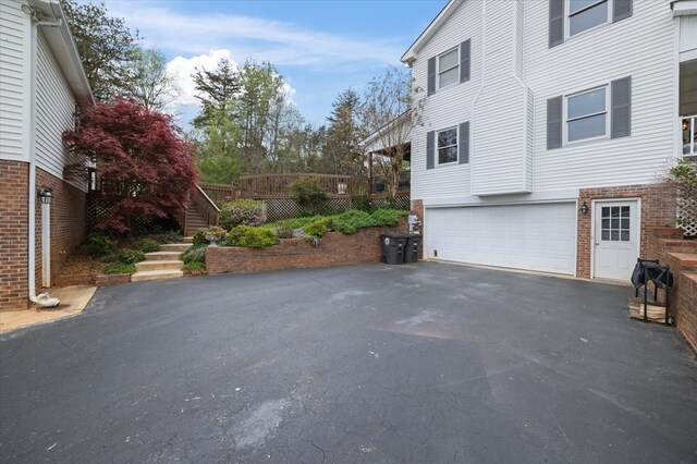 view of side of property featuring brick siding, driveway, stairway, and an attached garage