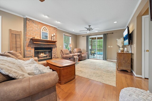 living room featuring light wood-type flooring, a brick fireplace, ceiling fan, and crown molding