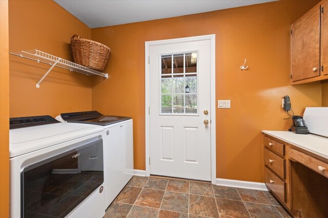 laundry area featuring stone finish floor, washing machine and dryer, cabinet space, and baseboards