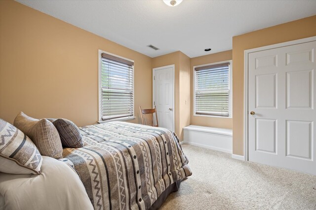 carpeted bedroom with visible vents, baseboards, and multiple windows