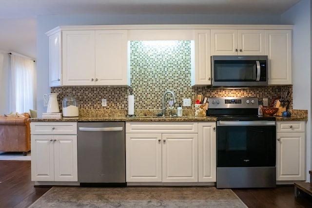 kitchen featuring dark wood finished floors, dark stone counters, a sink, appliances with stainless steel finishes, and white cabinetry