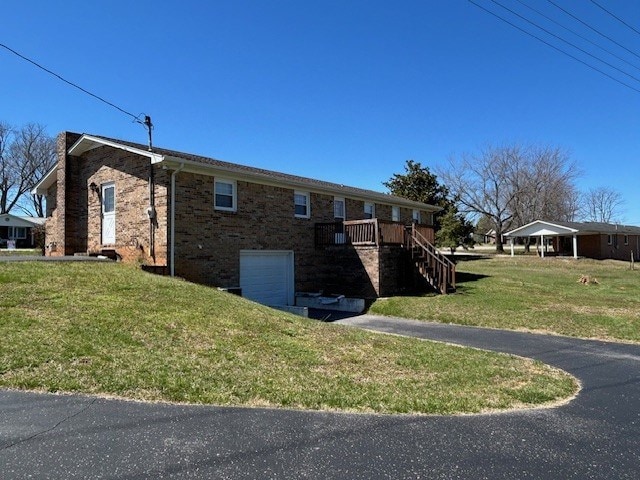 view of side of home with stairs, driveway, brick siding, a lawn, and a garage
