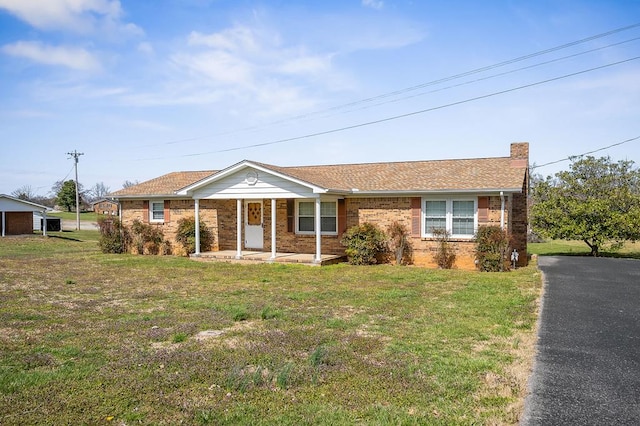 ranch-style house featuring brick siding, a chimney, a front lawn, and covered porch