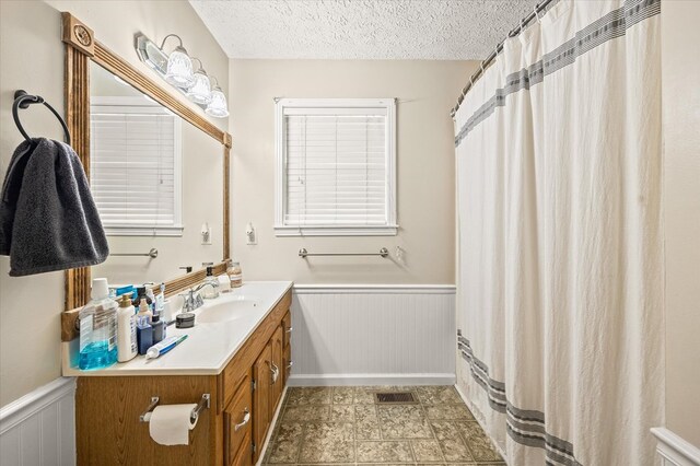 full bathroom with a wainscoted wall, a textured ceiling, vanity, and visible vents