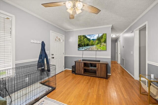 living area featuring a textured ceiling, wood finished floors, visible vents, baseboards, and ornamental molding