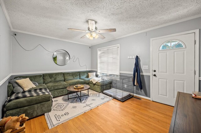 living area featuring ceiling fan, a textured ceiling, ornamental molding, and wood finished floors