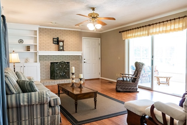 living area with baseboards, wood finished floors, crown molding, a textured ceiling, and a fireplace