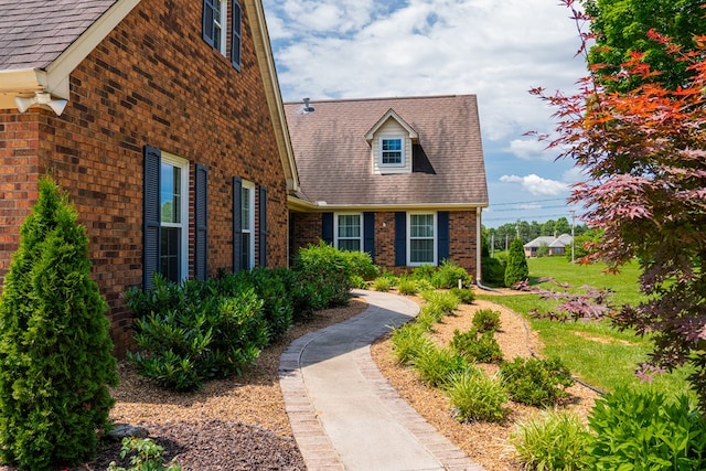 exterior space with brick siding, roof with shingles, and a front lawn