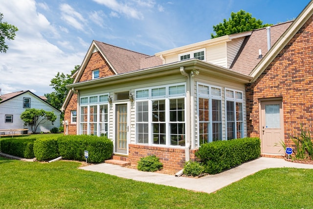 view of front of property featuring a sunroom, brick siding, a front lawn, and roof with shingles