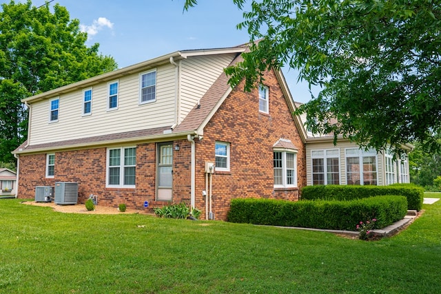 view of front of property with central air condition unit, a shingled roof, a front yard, and brick siding