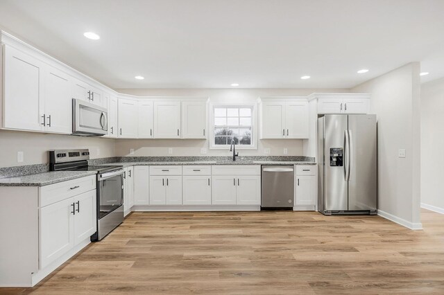 kitchen with stainless steel appliances, white cabinets, a sink, and light stone countertops