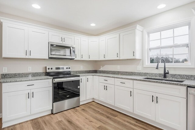 kitchen featuring stainless steel appliances, light wood-style floors, white cabinetry, a sink, and light stone countertops