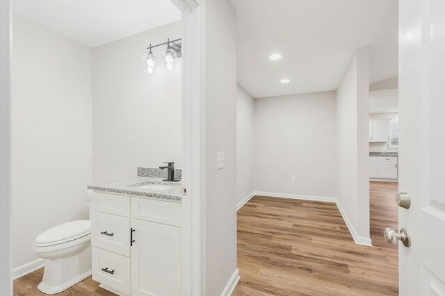 bathroom with recessed lighting, toilet, vanity, wood finished floors, and baseboards