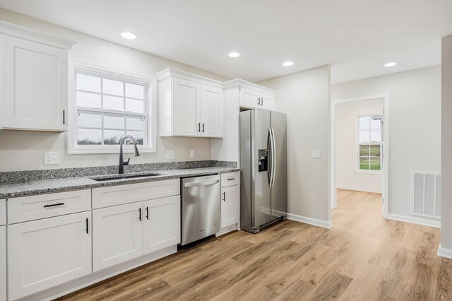 kitchen with light wood-style flooring, stainless steel appliances, a sink, visible vents, and white cabinets