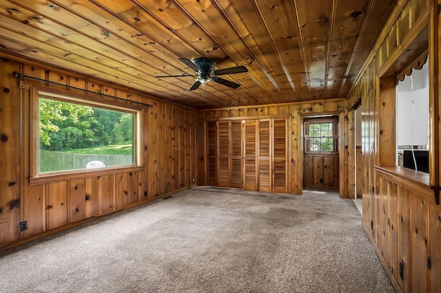 carpeted empty room with ceiling fan, wood ceiling, and wooden walls